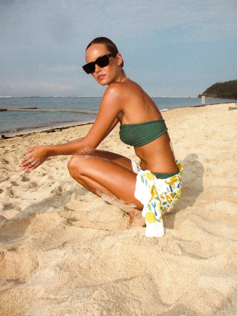 Woman in a green bandeau bikini on the sand with a citrus-print cloth tied at the waist